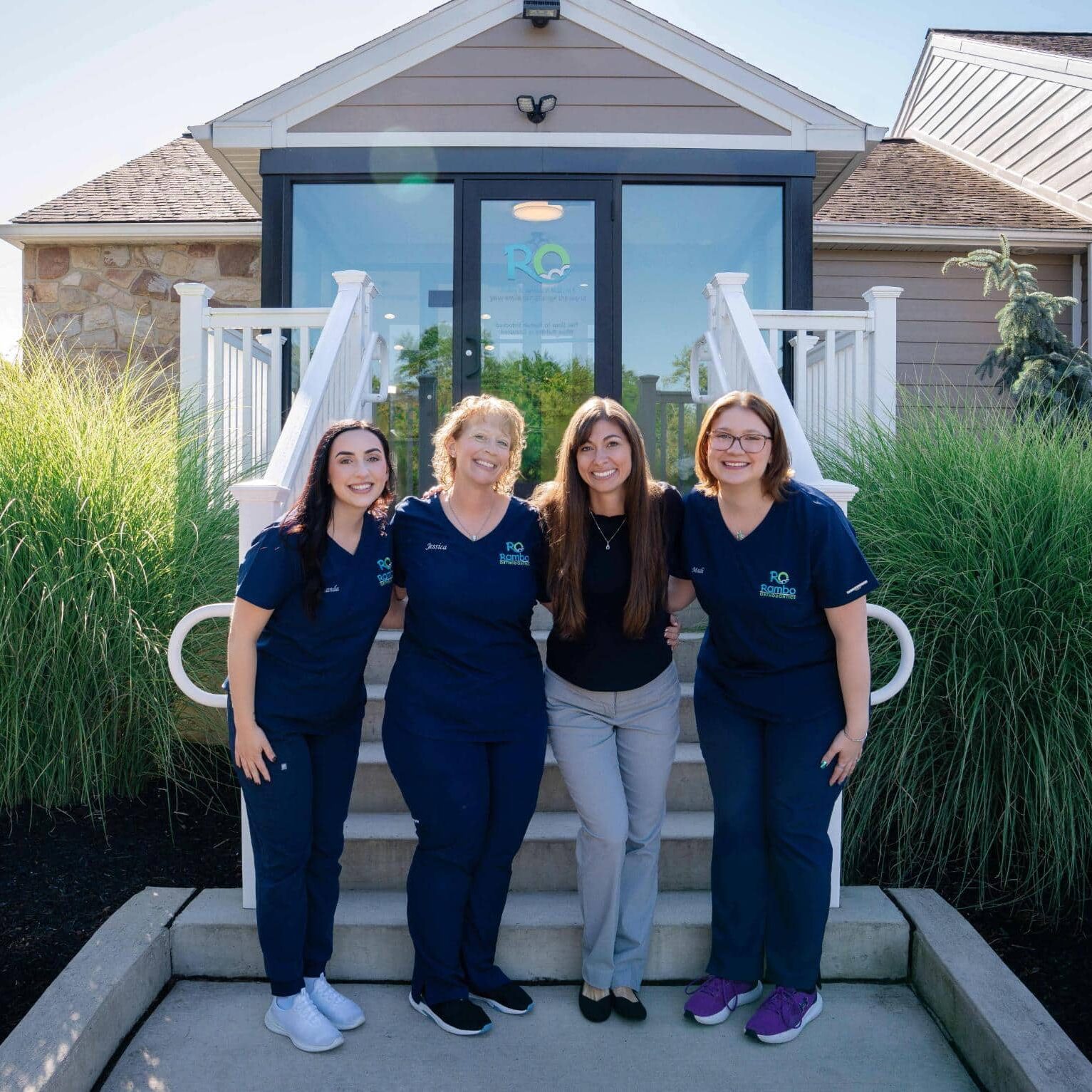 rambo-team-01816-02155 Rambo Orthodontics team members smiling on steps outside the office, showcasing a welcoming environment and personalized care approach.